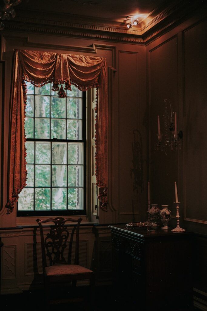 Antique chair by window with ornate drapes and chandelier