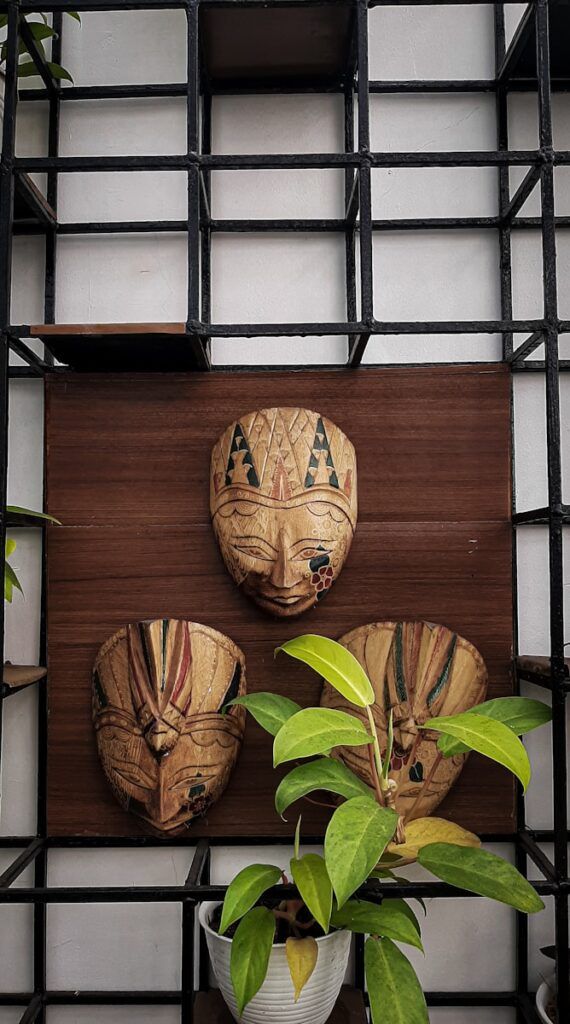 a couple of masks on a wall near a potted plant