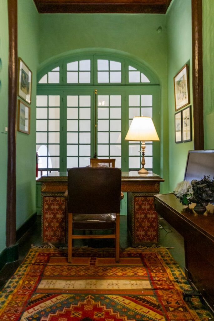 A room with a desk, chair, lamp and pictures on the wall