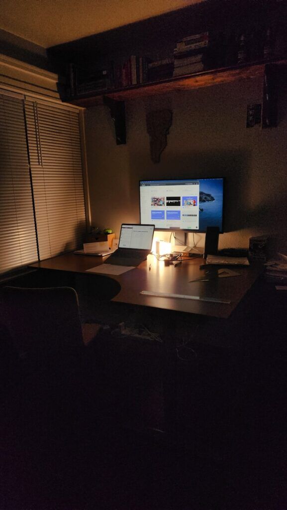 A dimly lit desk with a laptop and monitor.