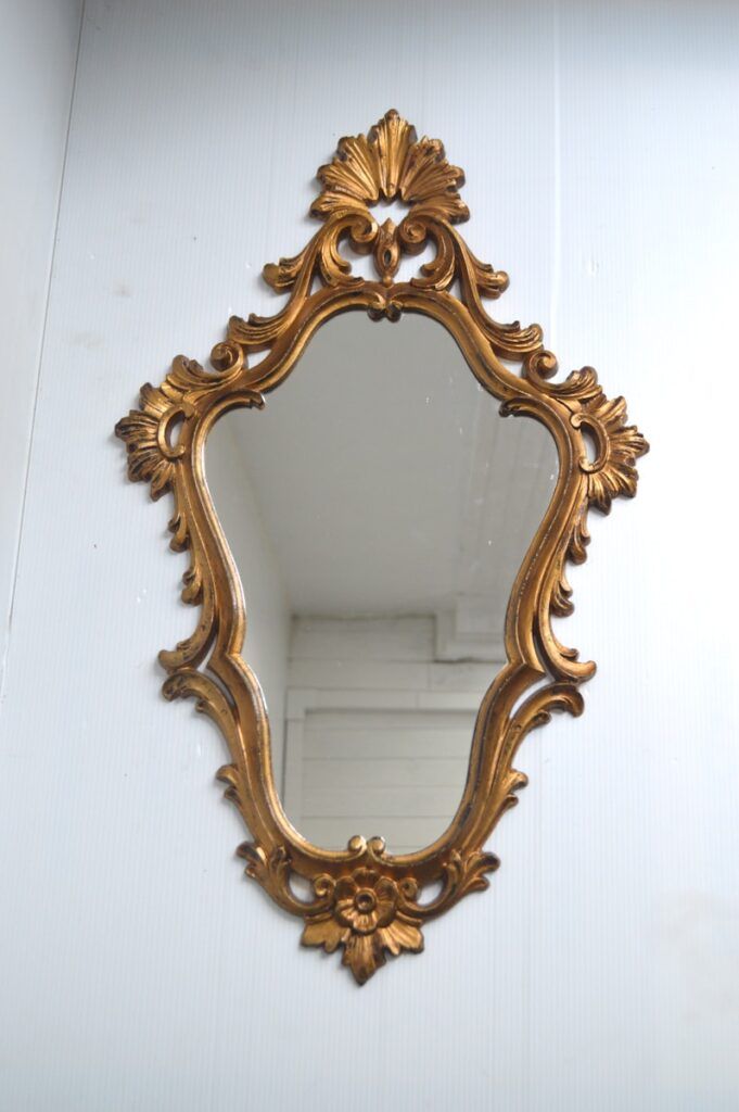 A gilded mirror hanging on a wall next to a white wall