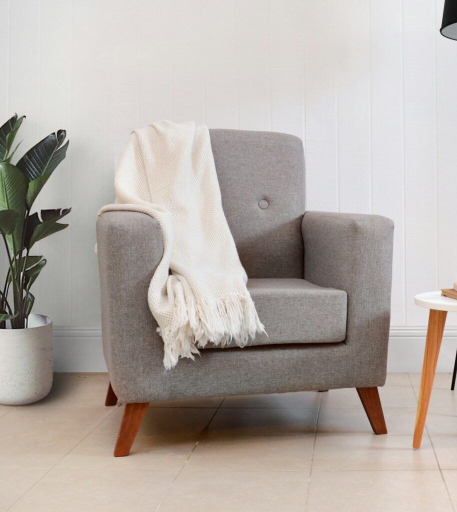 A gray armchair with a cream blanket draped over it.
