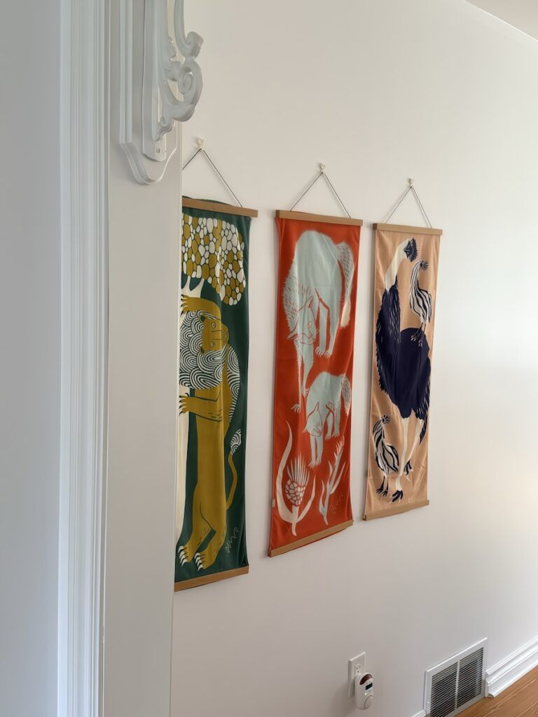 Three animal tapestries hanging on a white wall.