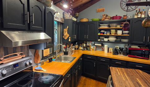 rustic kitchen including a butcher block island, oak counter tops, and black cabinets.